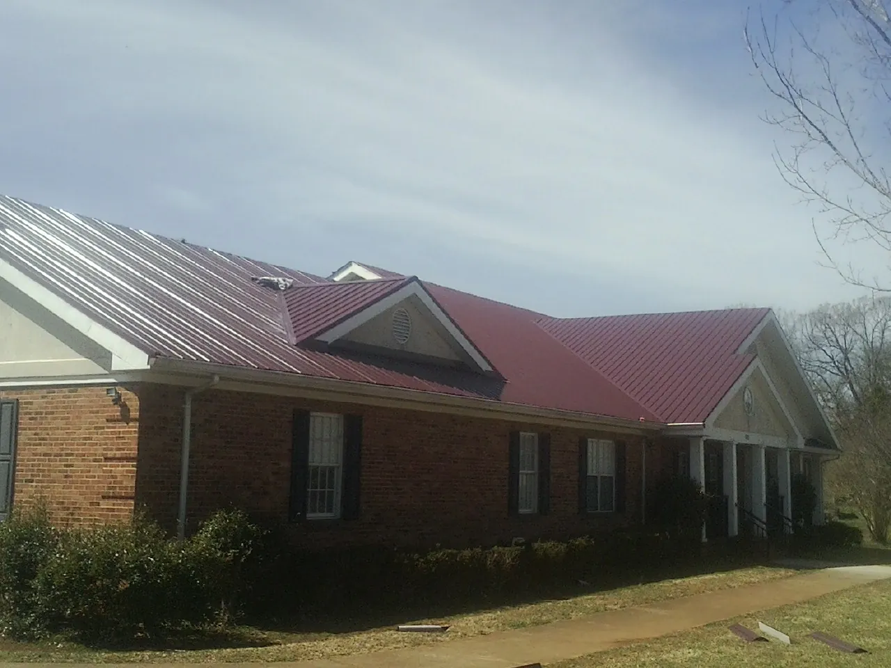 Red metal roof with gabled entries on a long brick building, from a Hail Damage Roof Repair job in Disputanta