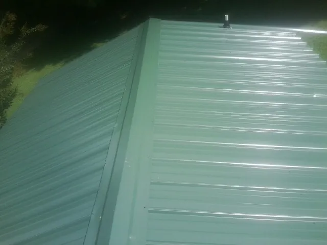 New green metal panels meeting at the ridge of a roof — Flat Roof Repair work by our crew in Disputanta