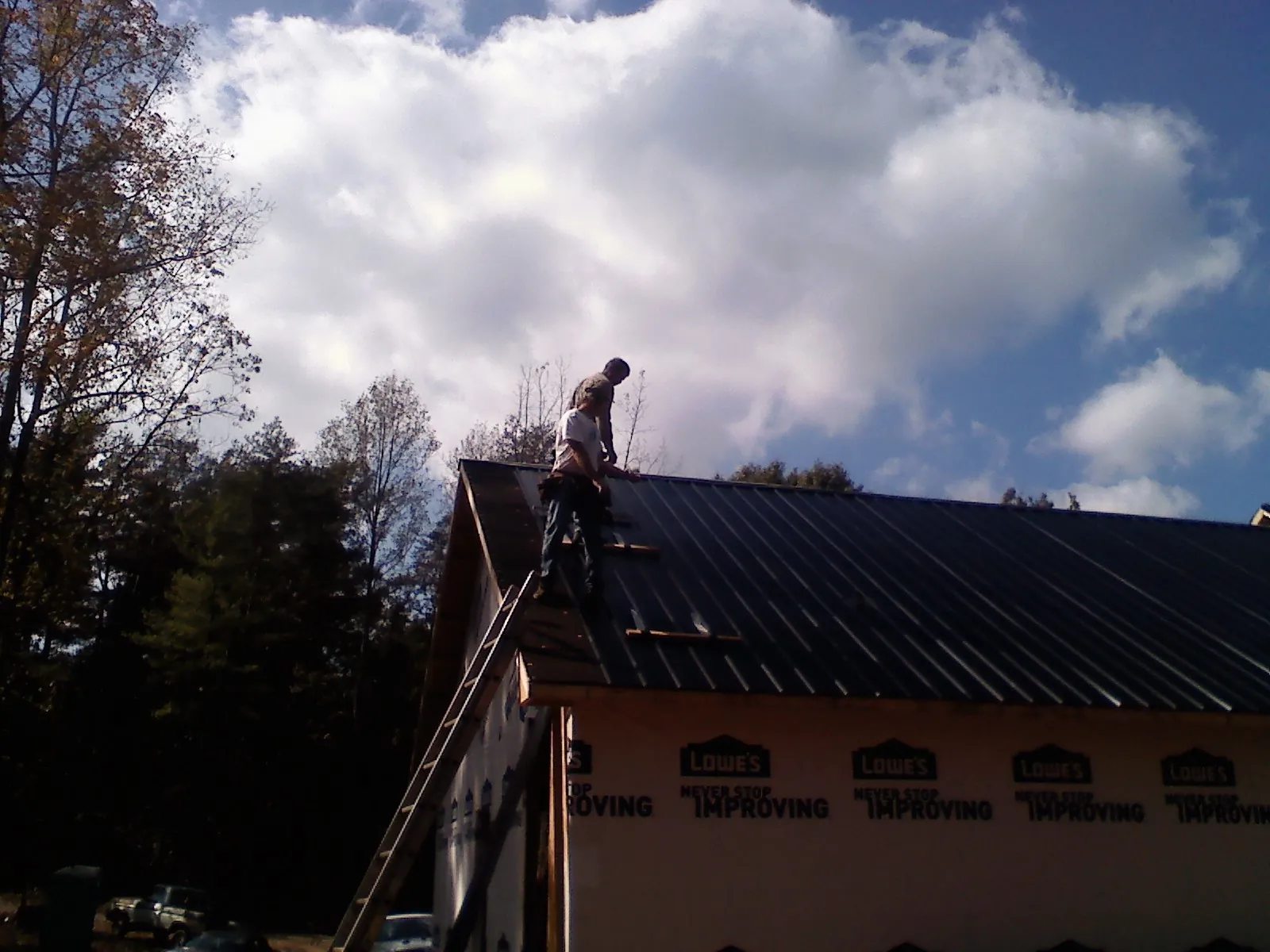 Roofer fastening dark metal panels high against a cloudy sky, from a Roof Inspection job in Disputanta